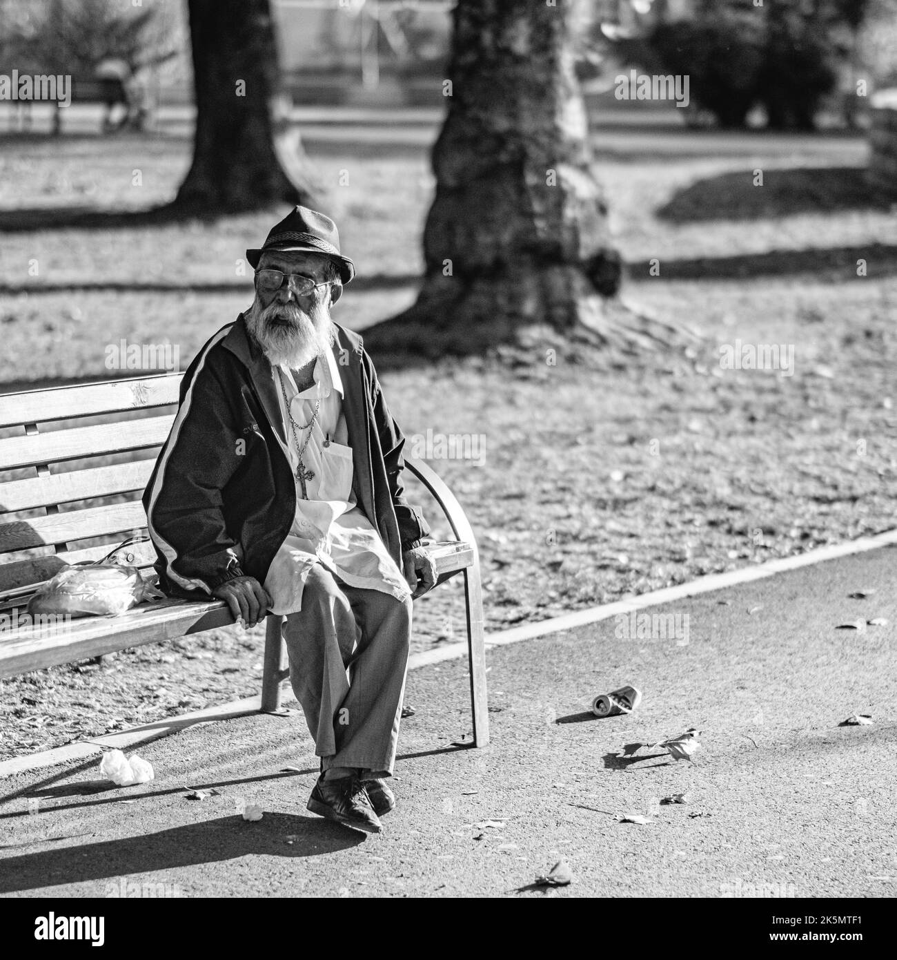 A greyscale shot of an old man sitting on the bench in park Stock Photo