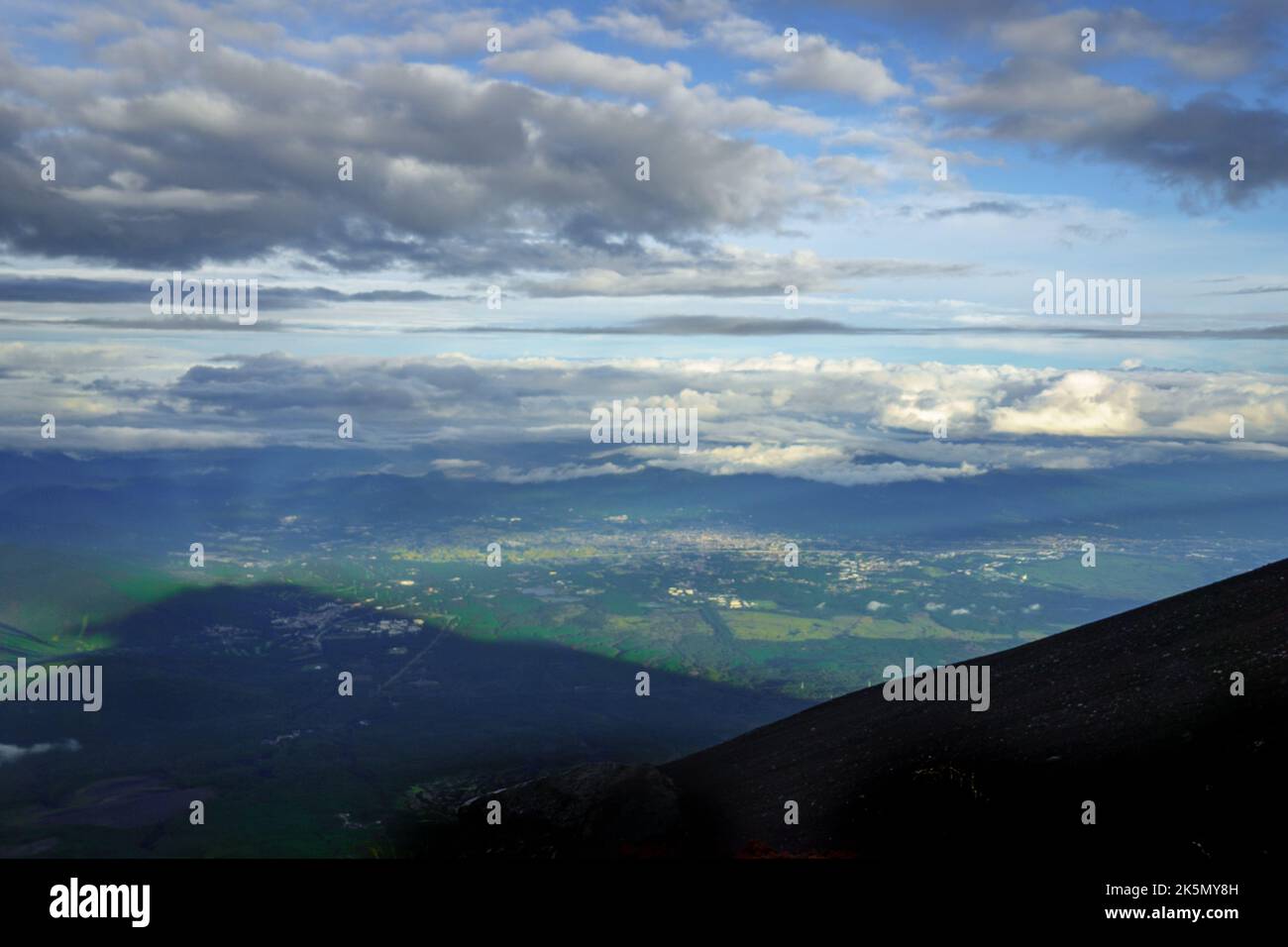 Mt. Fuji slope and large shadow over landscape on partly cloudy afternoon near peak Stock Photo