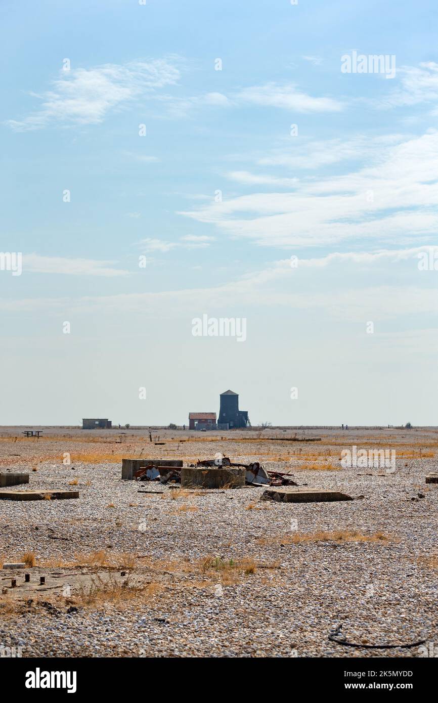 Flat shingle landscape with debris and buildings in the distance, Orford Ness, Suffolk, England Stock Photo