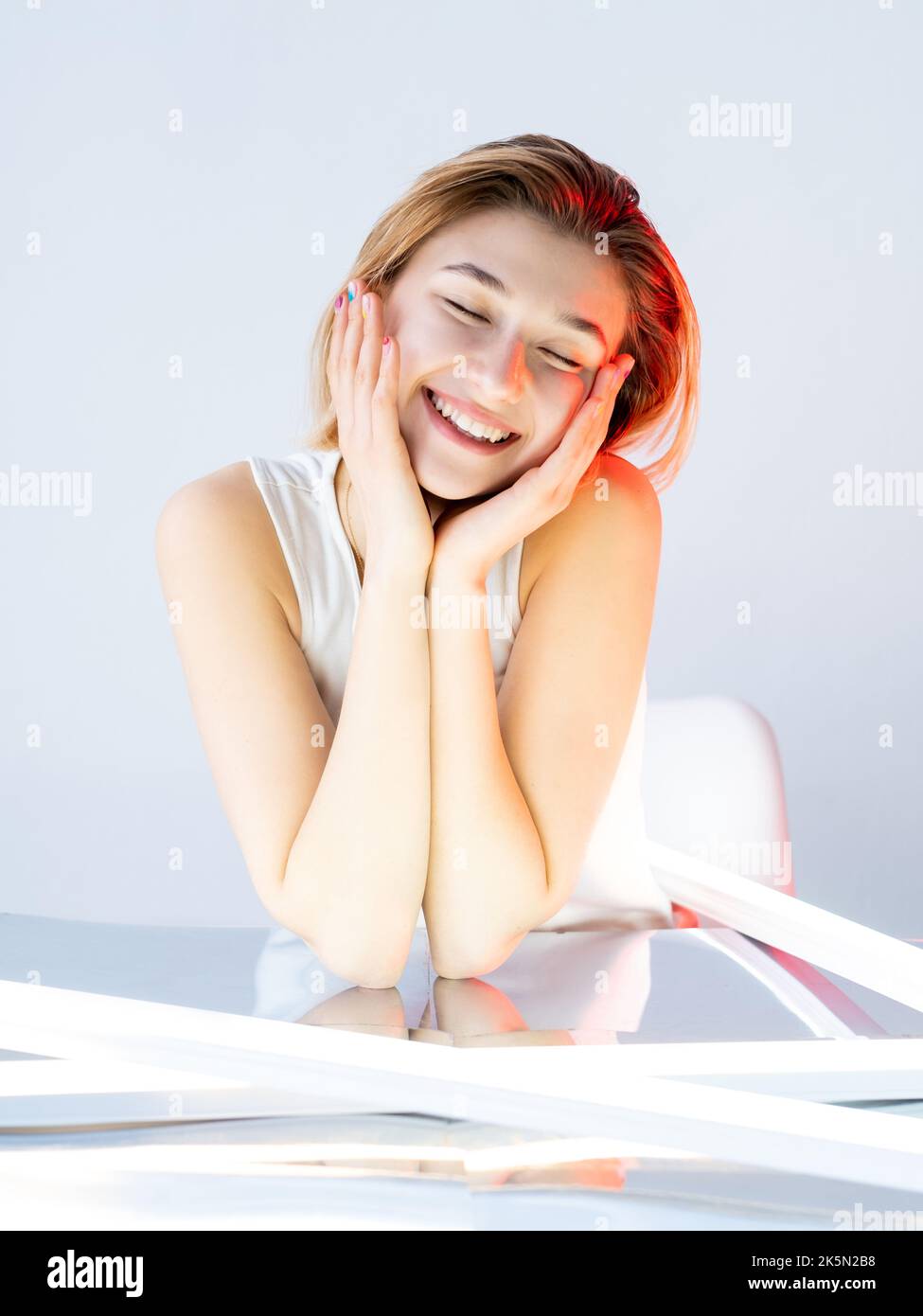 Beauty portrait. Facial care. Moisturizing nourishing. Happy satisfied smiling girl enjoying touching soft fresh face skin in red neon light isolated Stock Photo