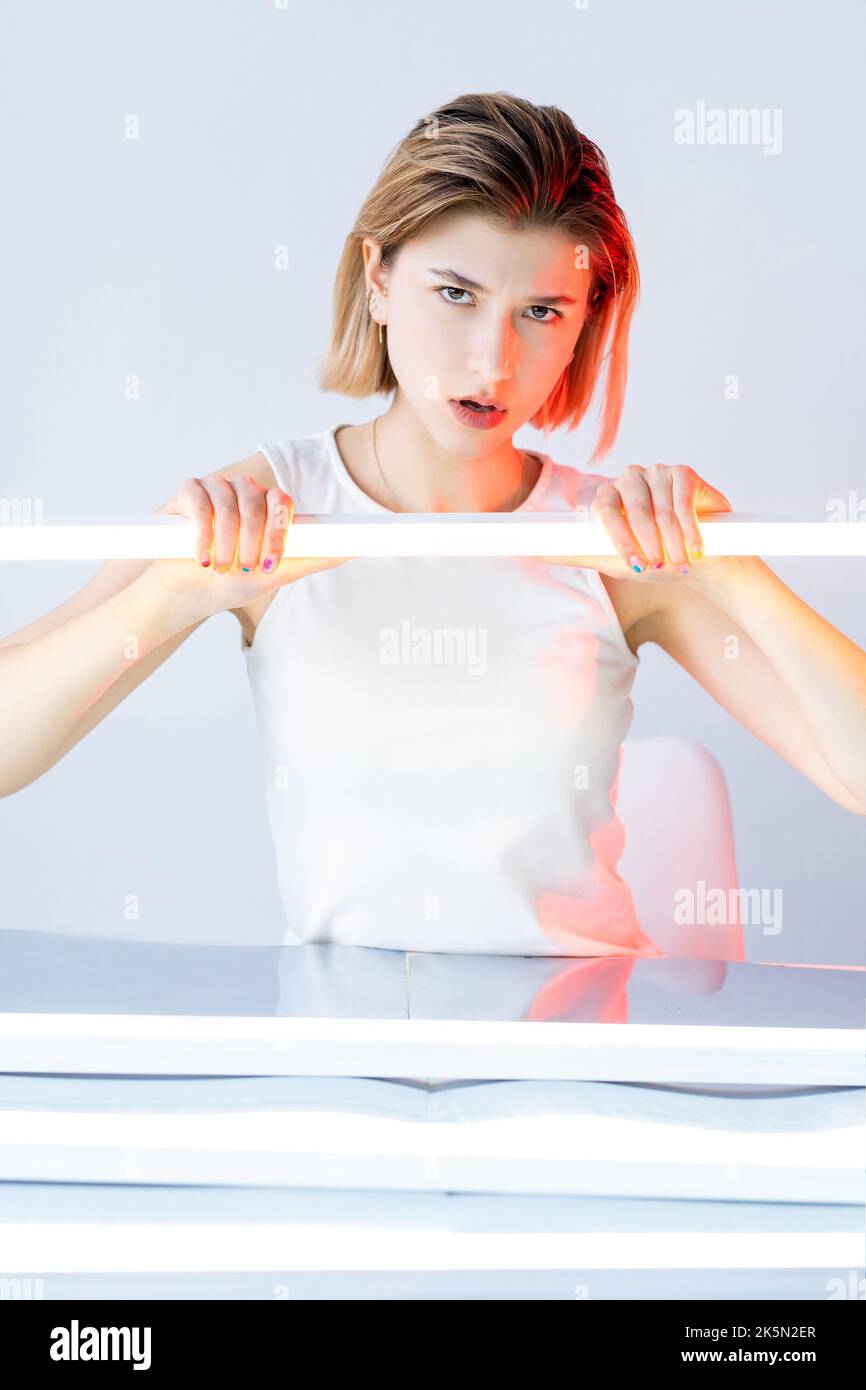 Annoyed woman. Futuristic portrait. Conflict anger. Red color neon light displeased disturbed skeptic girl face with white led lamp glow isolated on n Stock Photo