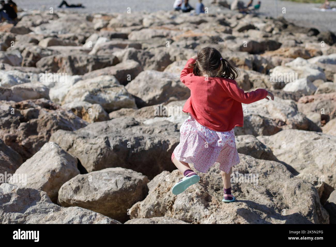 Little girl jumping on rocks on the French riviera during a sunny spring day. Stock Photo