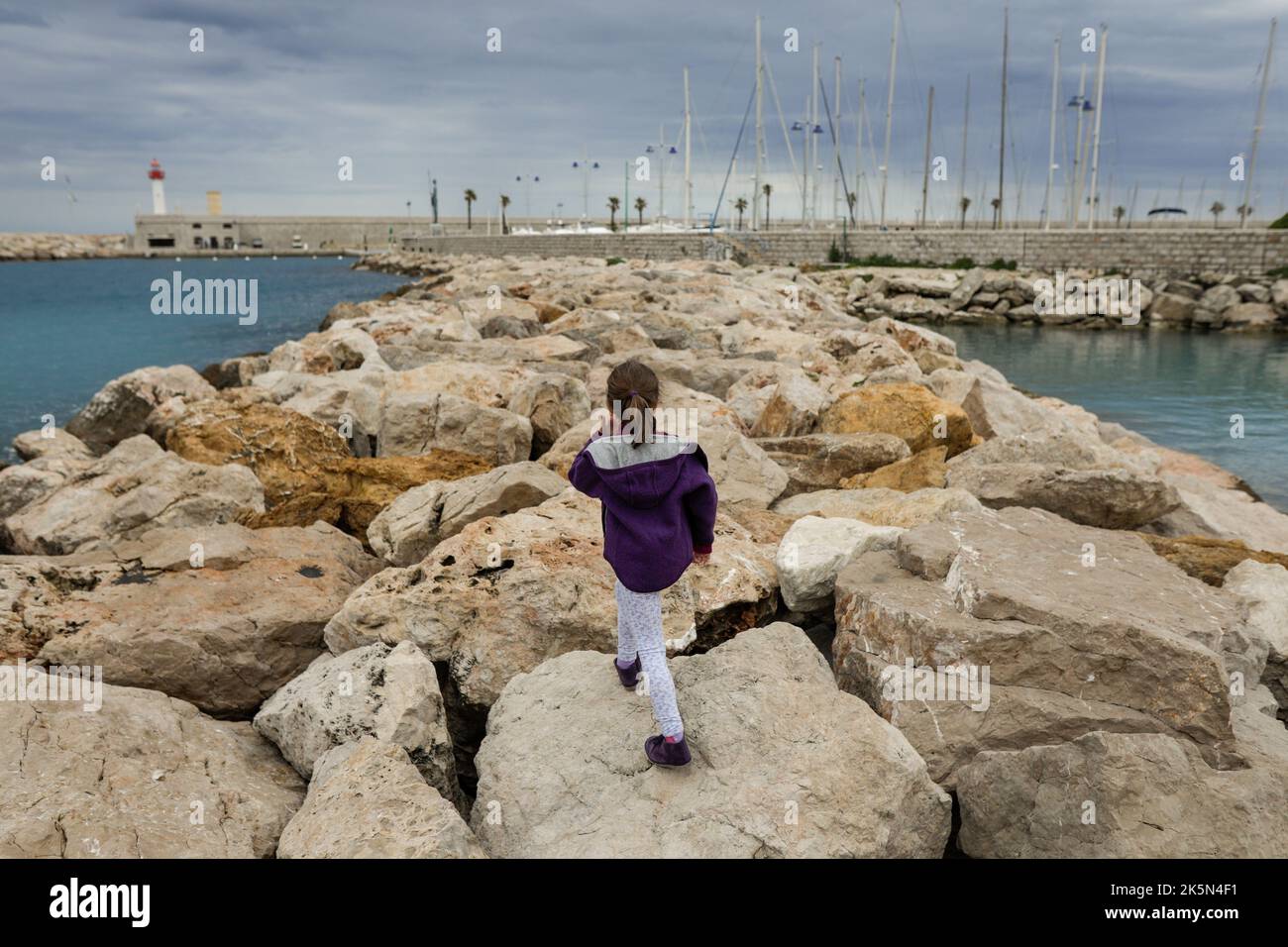 Little girl jumping on rocks on the French riviera during a cloudy spring day. Stock Photo