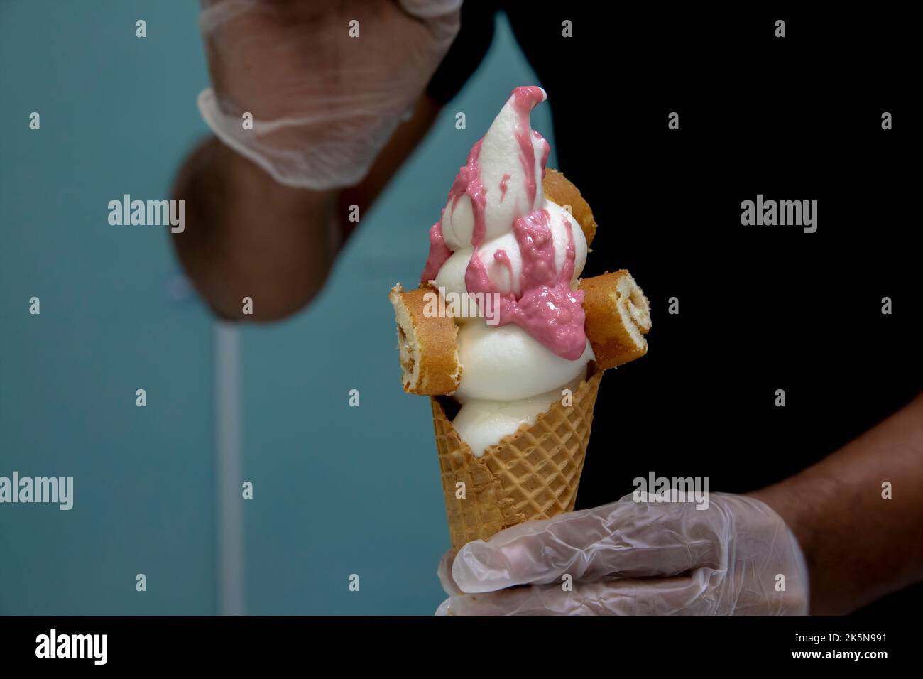 close-up of a man adding pink topping on a vanilla ice cream cone Stock Photo