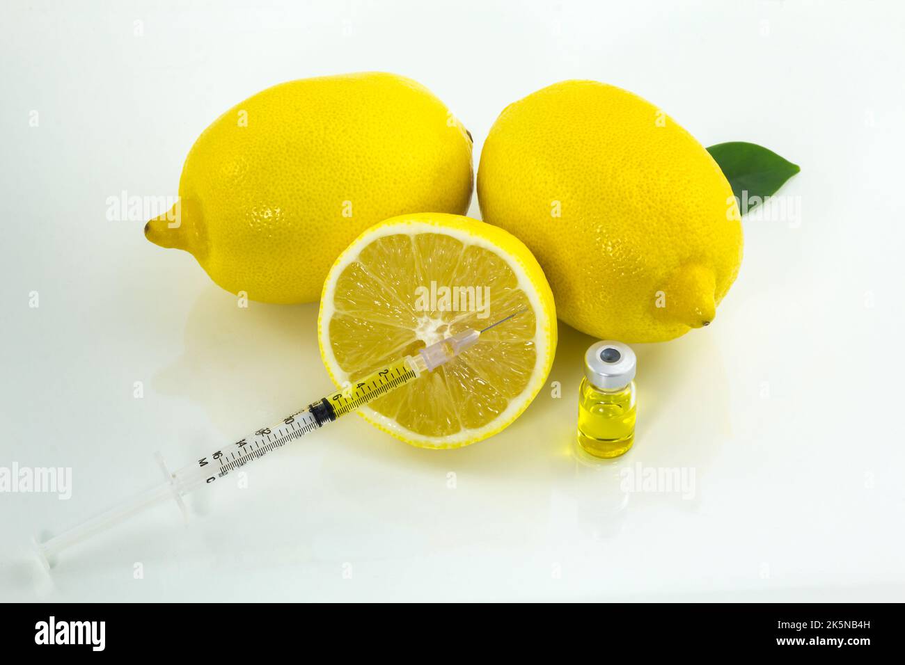Two and a half lemons with a syringe and a bottle of juice. Symbol of