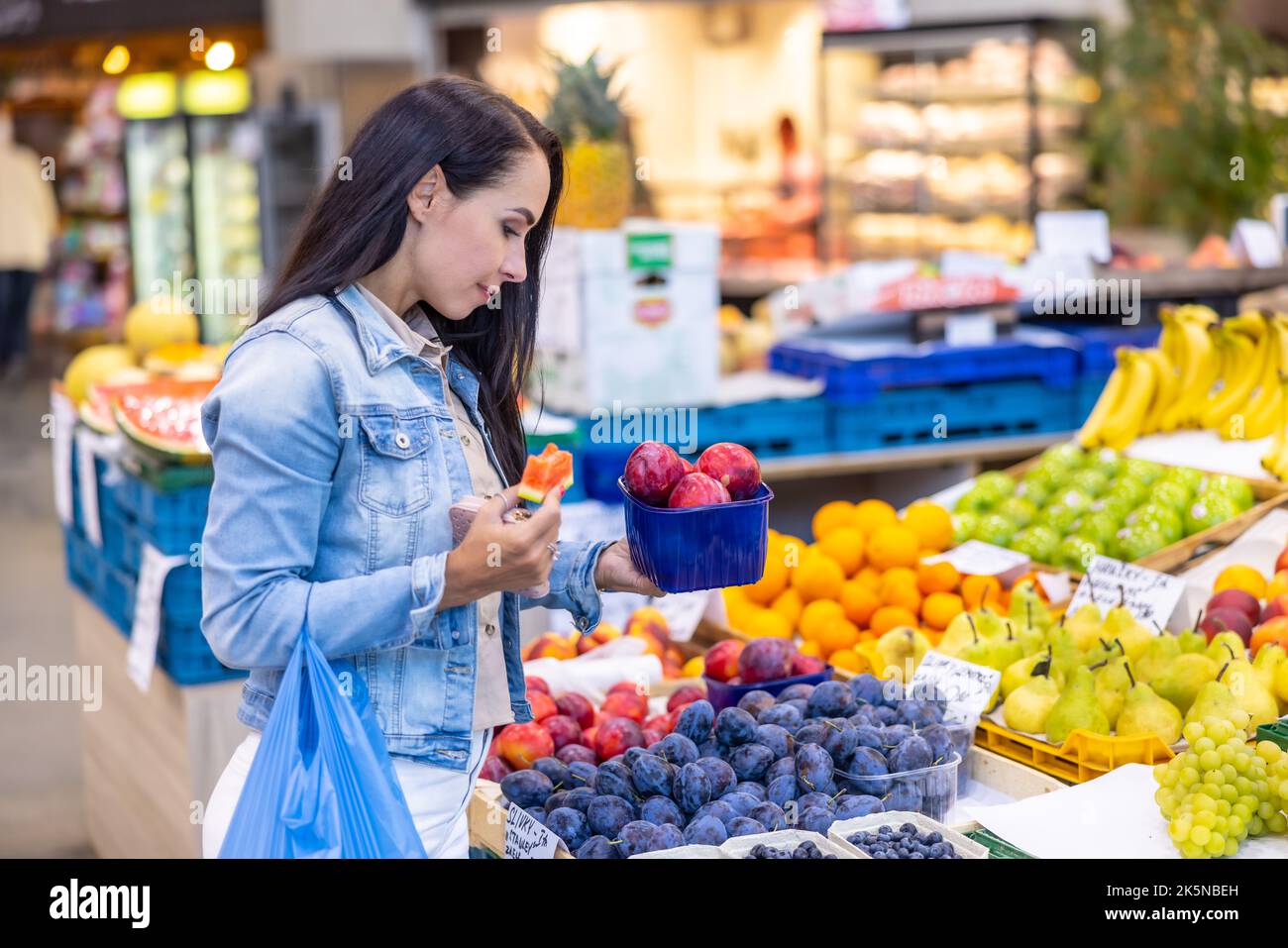 Woman picks a box of plums from fruits selection in the grocery store