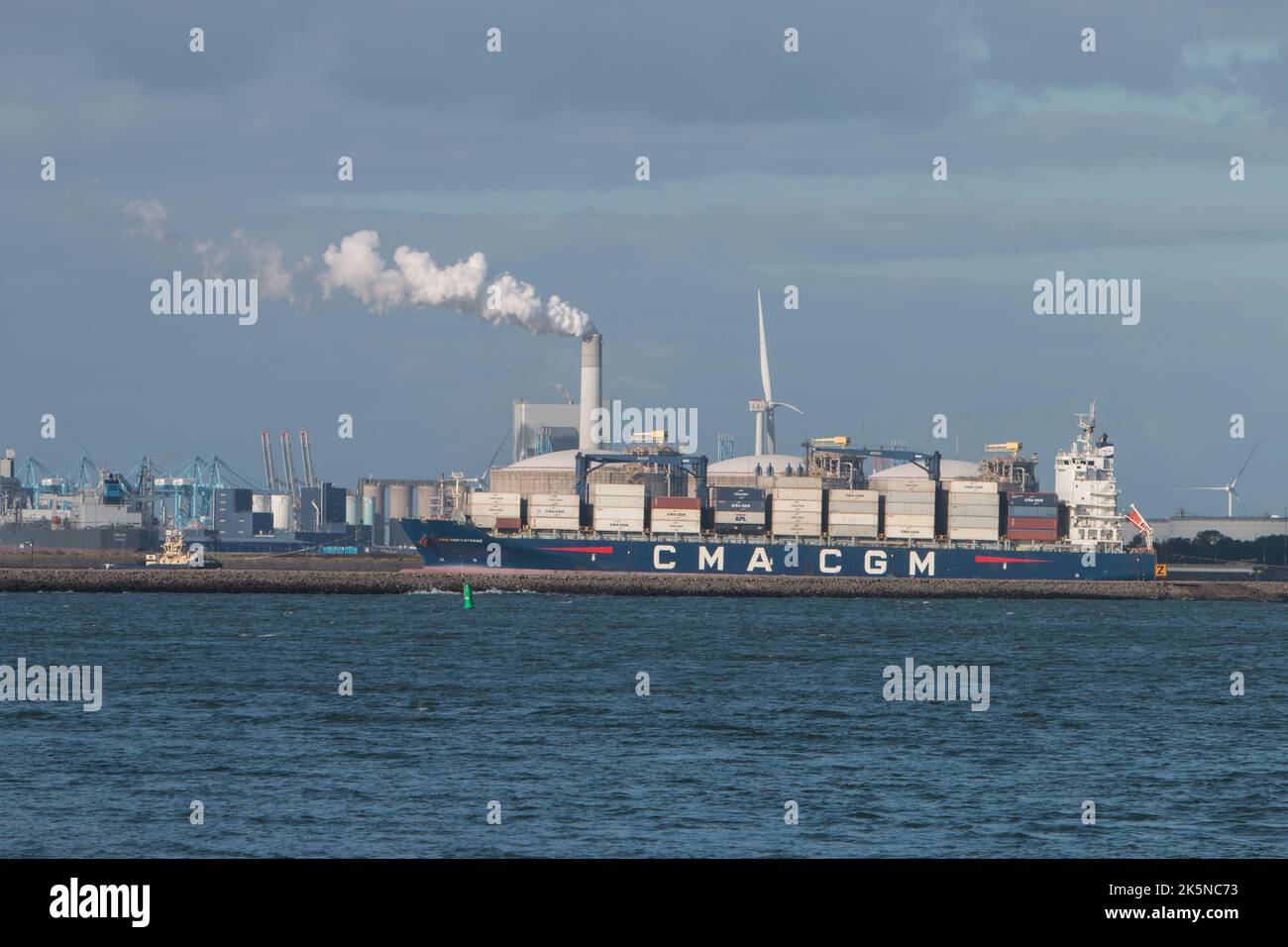Container ship with port and chimney in background. Viewed from the