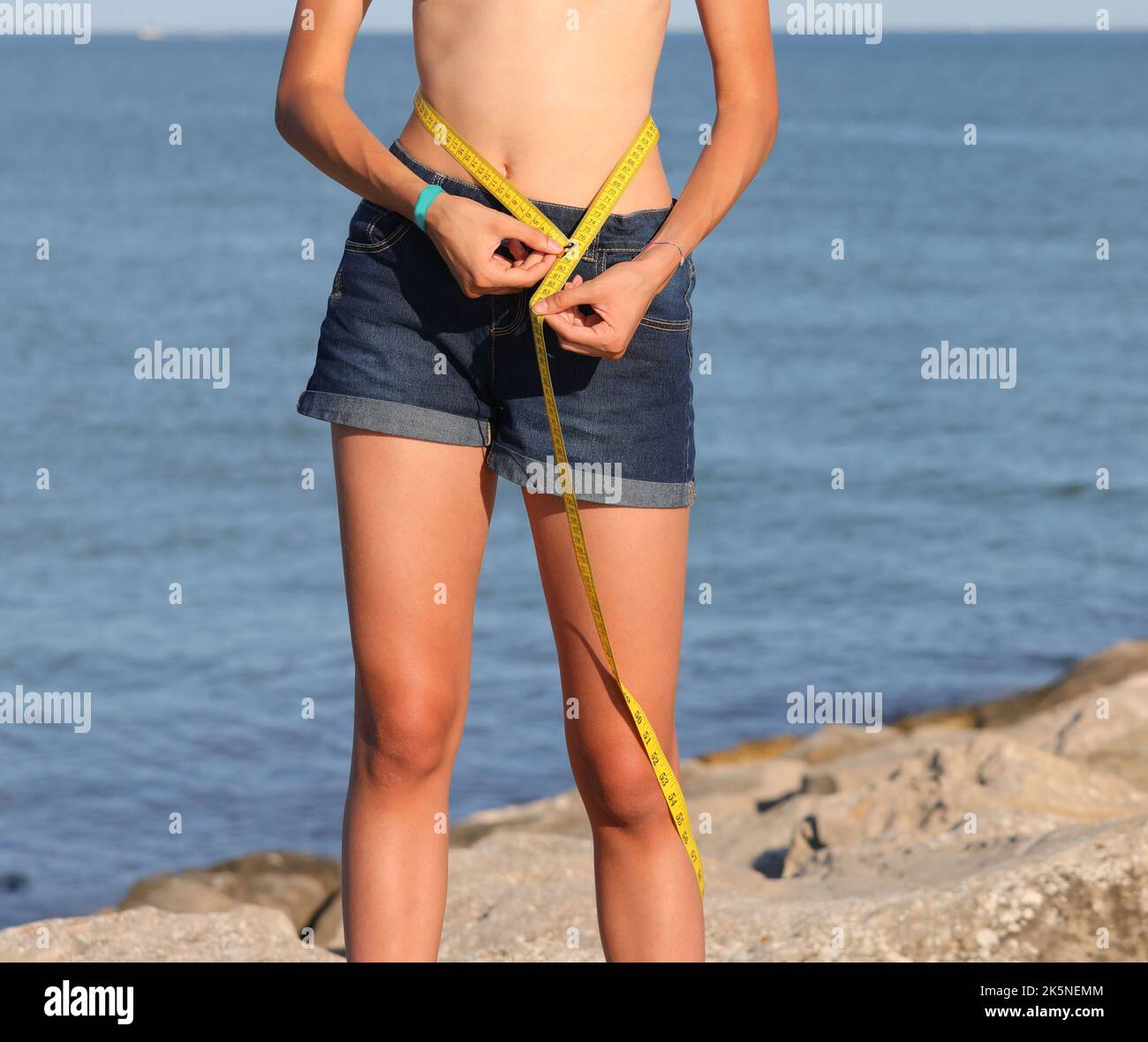 girl measures the waist d with jeans shorts in the summer by the sea