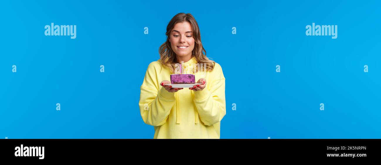 Celebration, party and lifestyle concept. Girl want have bite of tasty desert, holding b-day cake with lit candle as making wish, look with desire and Stock Photo