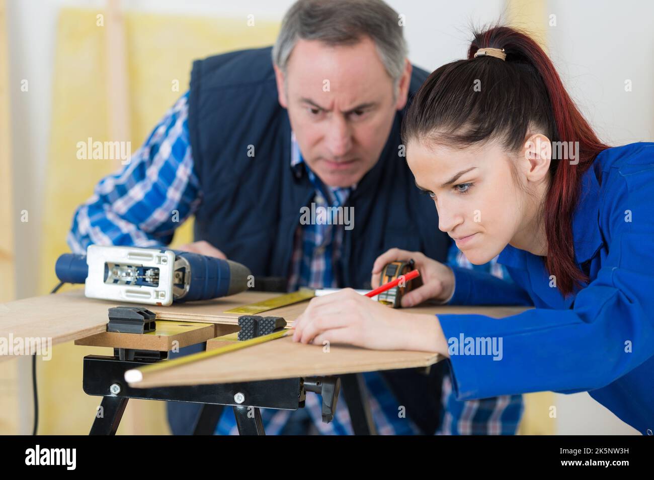 supervisor watching over female apprentice carpenter having difficulties Stock Photo