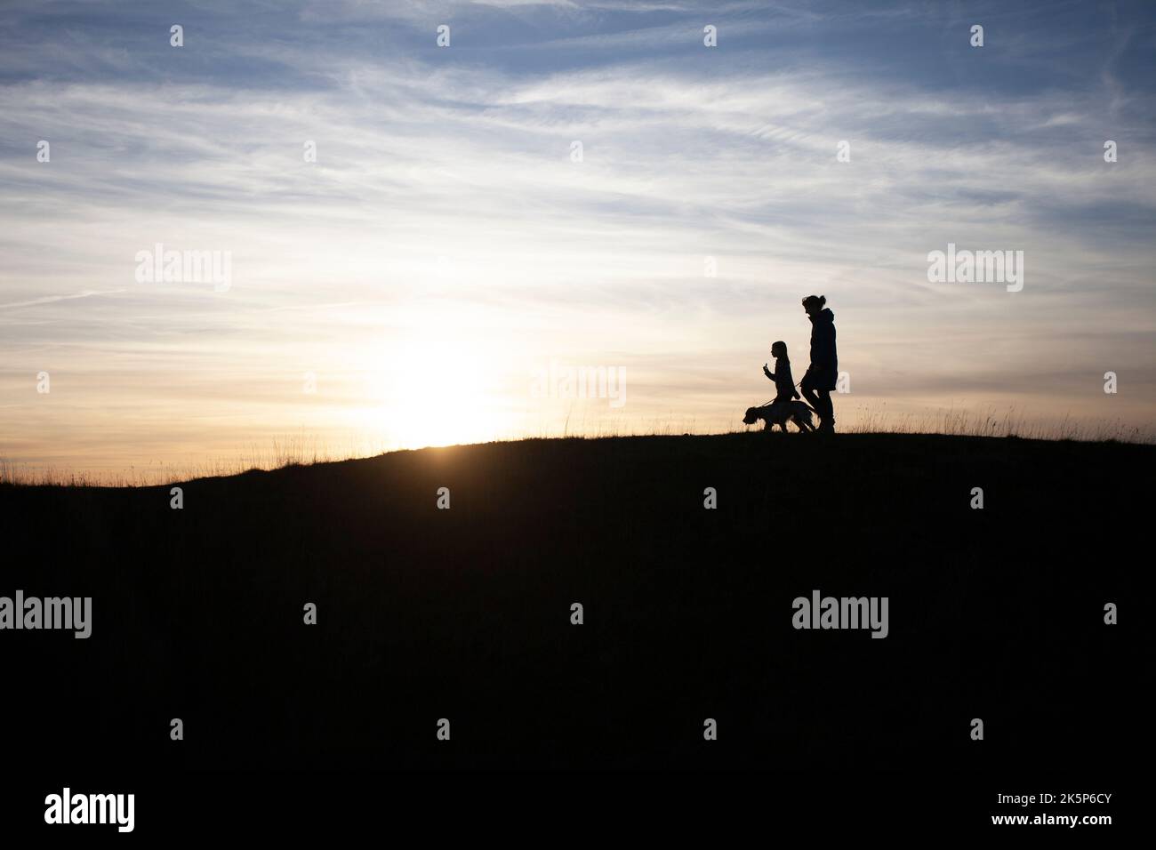 silhouette of people walking their dog Stock Photo
