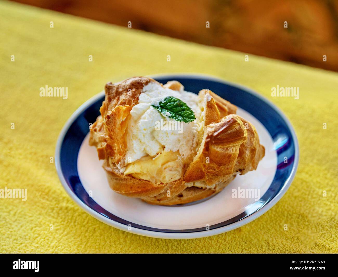 Light pastry dessert from battered dough with whipped cream and caramel cream on small plate on yellow background, closeup. Stock Photo