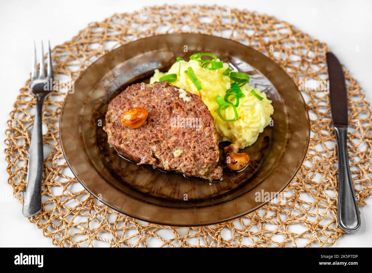 Baked minced beef, garlic and mashed potato on plate, cutlery and bamboo pad on table. Serving size, lunch or dinner. Stock Photo