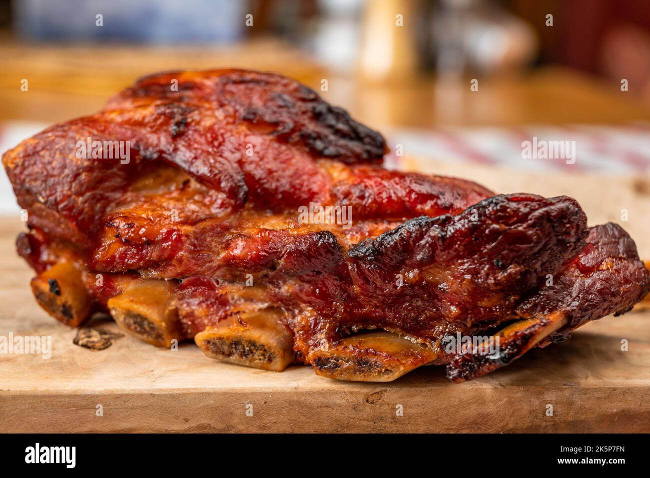 Good piece of juicy baked pork rib with crispy crust on wooden kitchen board on rustic table-cloth, closeup. Stock Photo
