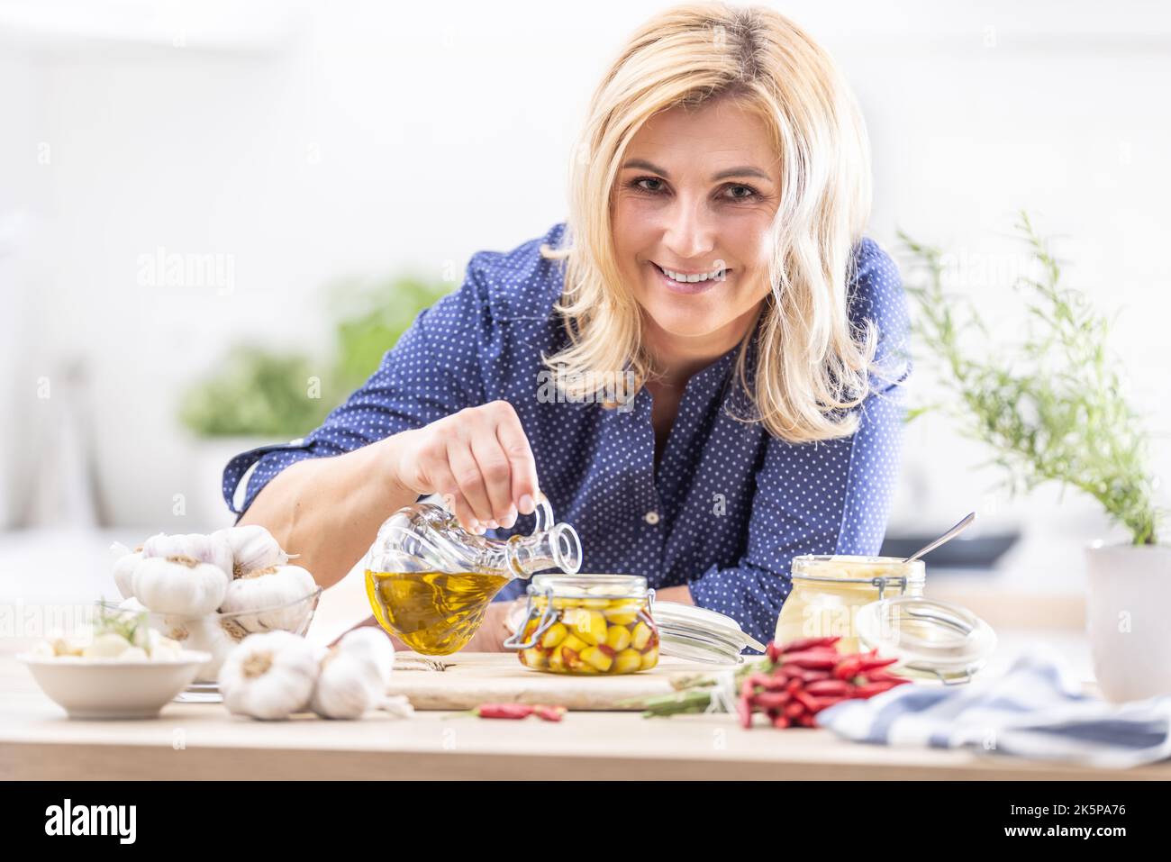 Woman pours oild over peeled garlic cloves to preserve them in a jar