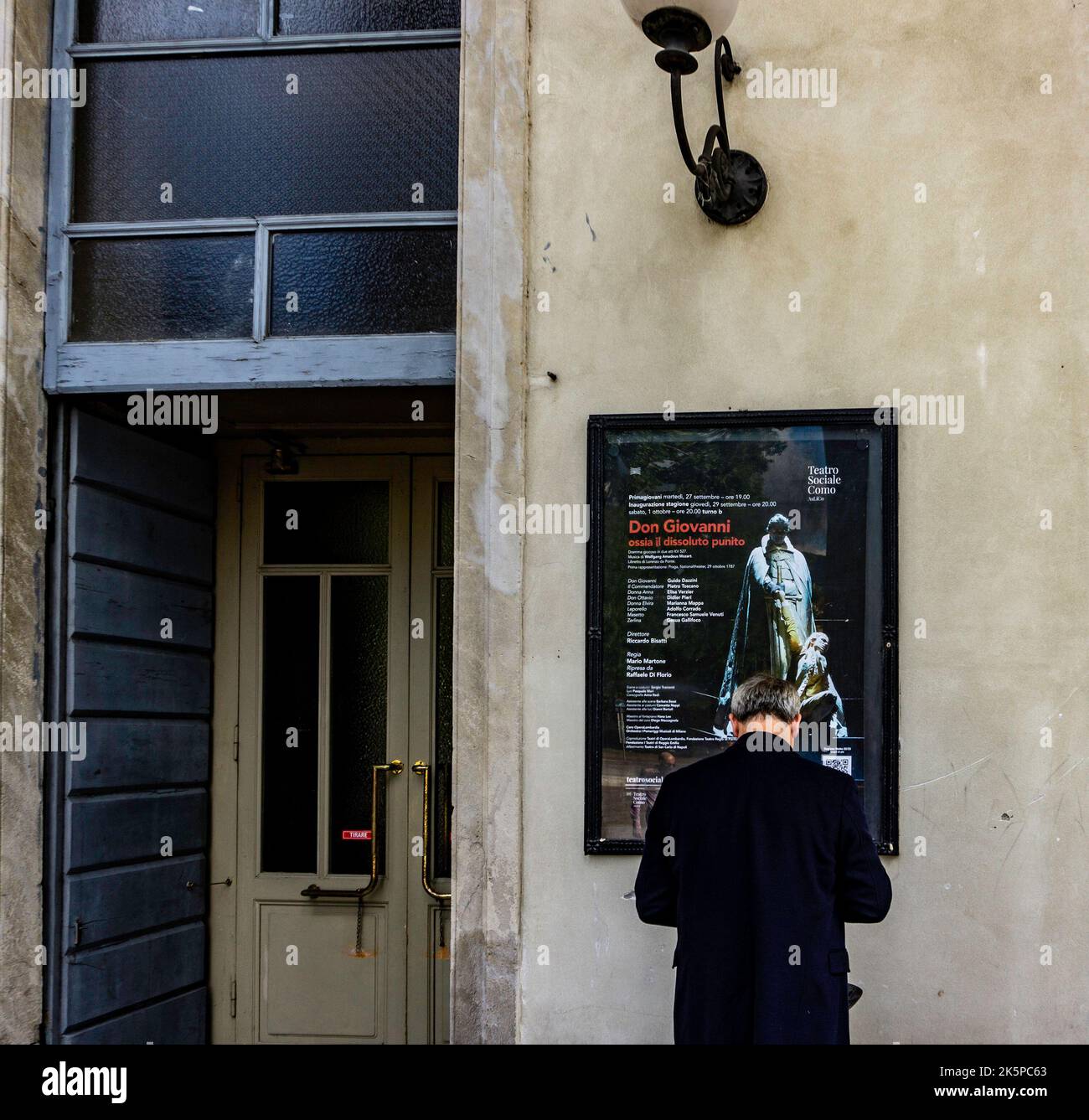 A man standing outside the opera house, Teatro Sociale Como, in Como, Italy. The poster is for a performance of Mozart’s Don Giovanni. Stock Photo
