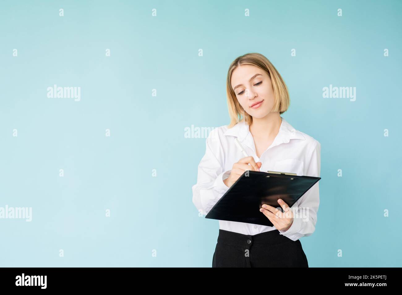 Business project. Happy woman. Important notes. Advertising background. Smiling office lady writing on clipboard in hands isolated blue copy space. Stock Photo