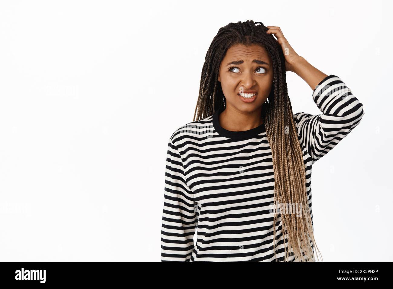 Portrait of confused black girl looking awkward and unsure, scratching head and looking aside with indecisive face expression, white background Stock Photo