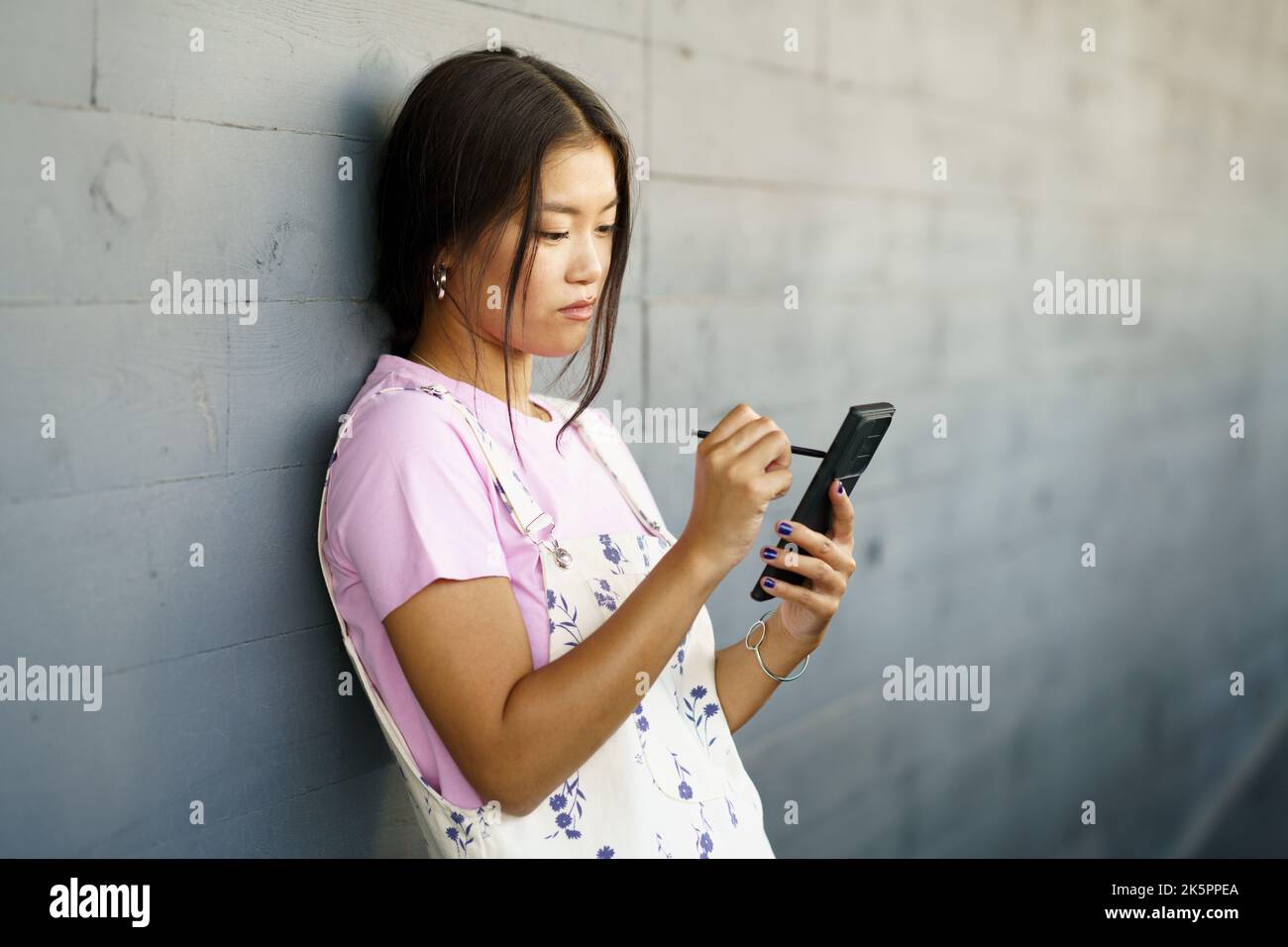 Serious Chinese girl using her smartphone with a pen or stylus,outdoors Stock Photo