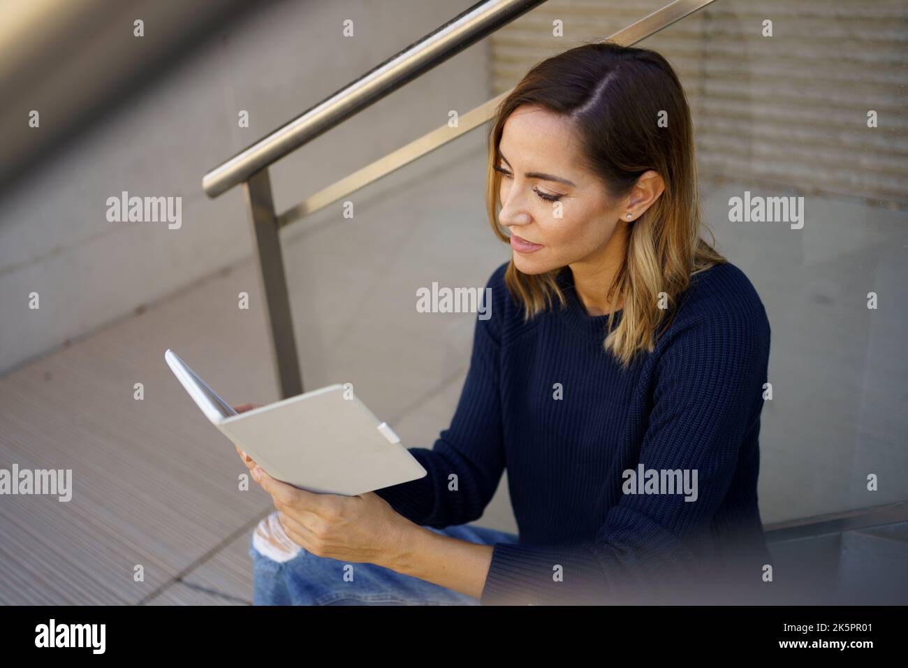 Middle-aged woman reading with her e-book on a coffee break near her office. Stock Photo