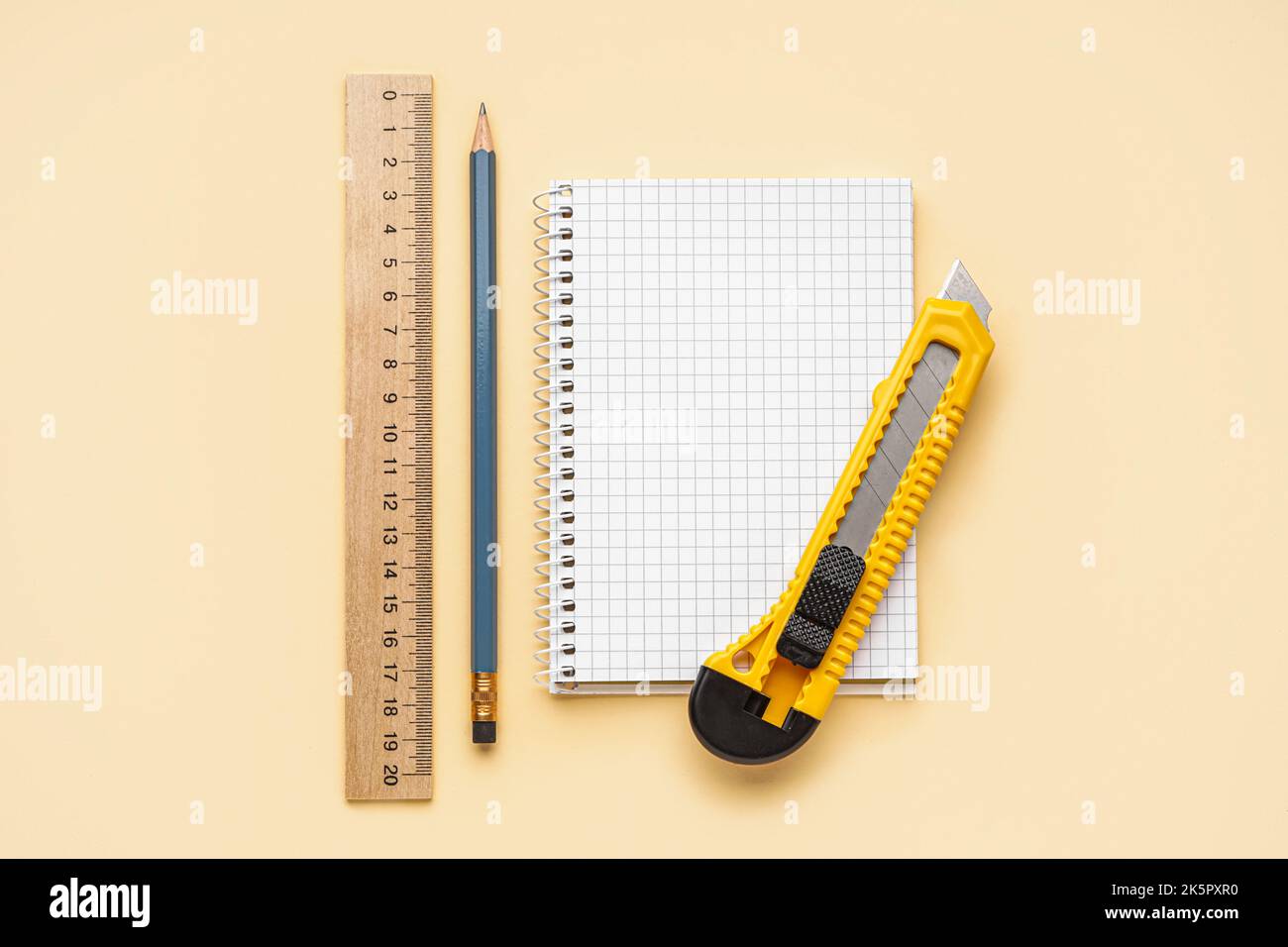 Utility knife with pencil, ruler and notebook on beige background Stock Photo