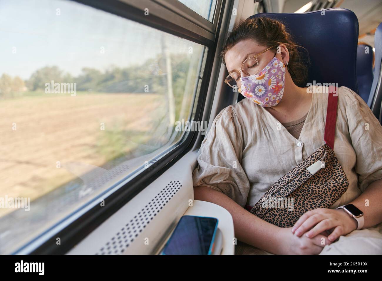 A girl with glasses in a medical mask sleeping on the train Stock Photo