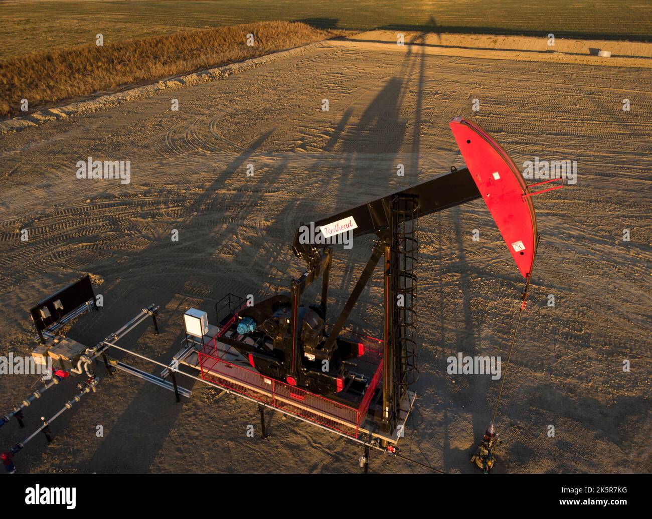 A pumpjack draws out oil and gas from a well head as the sun sets near