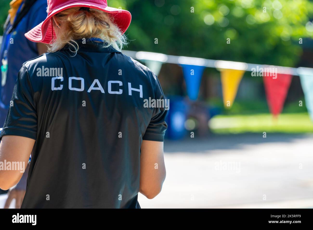 Back view of swimming coaches, wearing COACH shirt, working at an