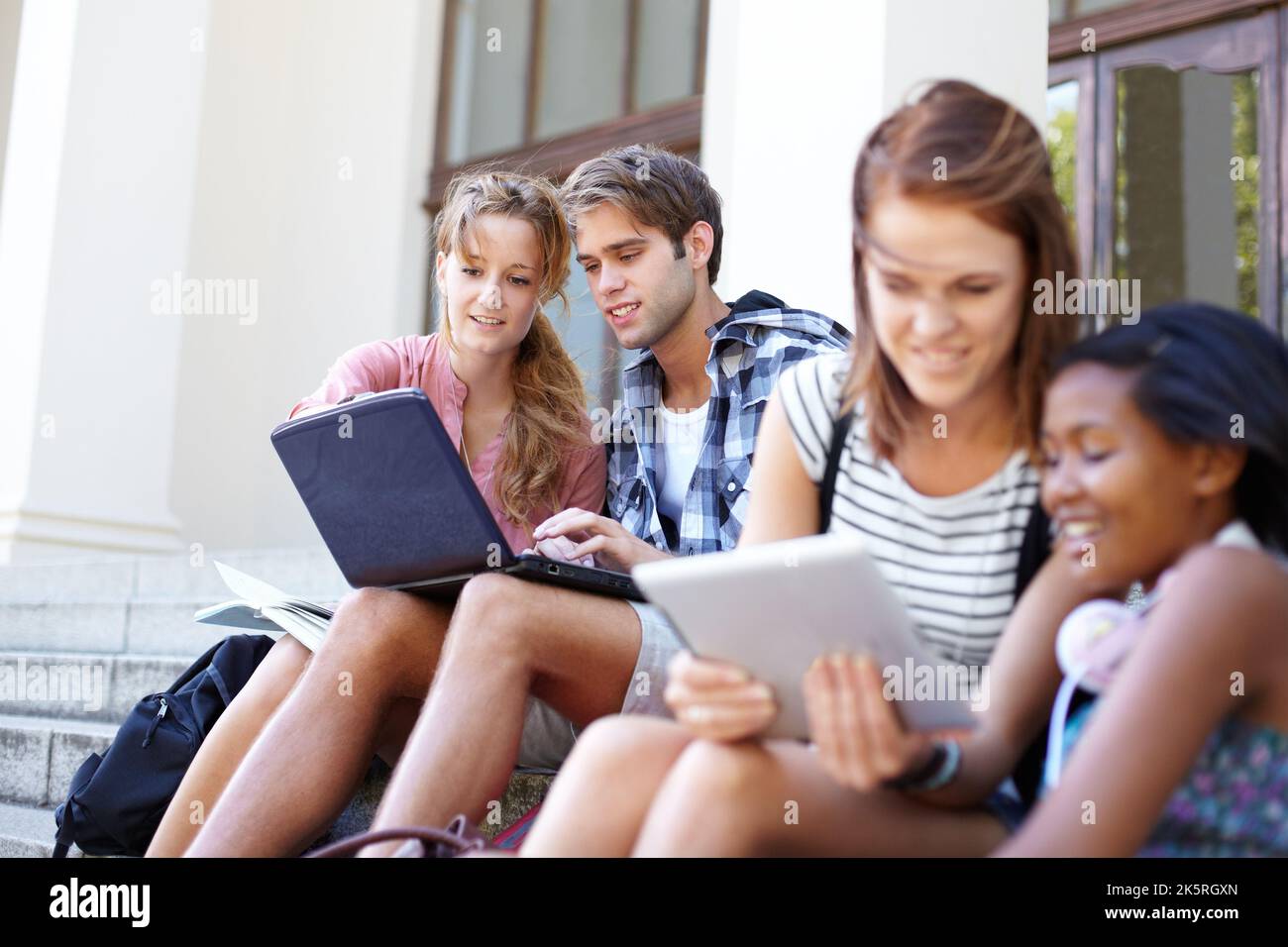 Tech savvy students. Young students on their laptops while outside of their college. Stock Photo