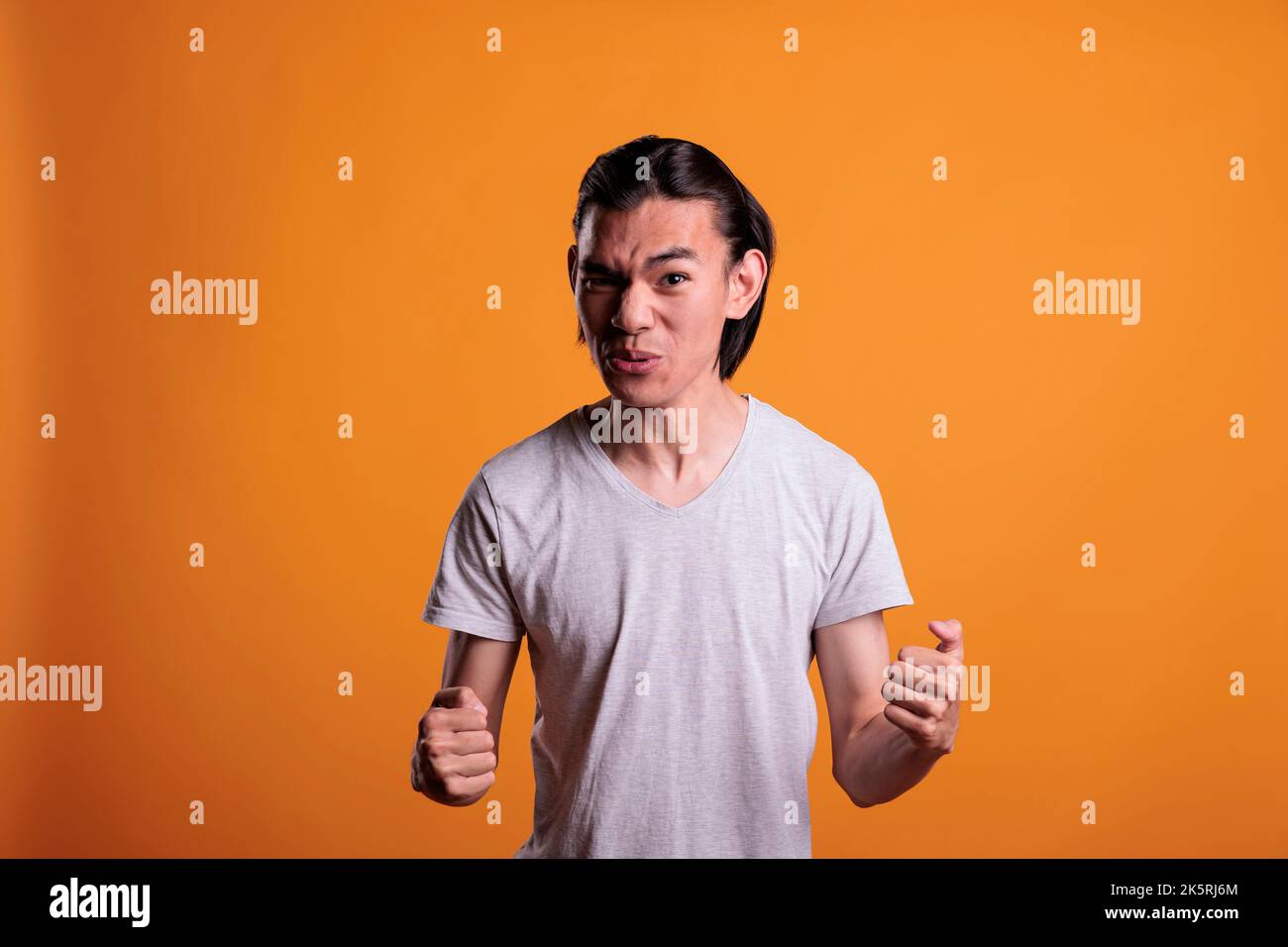 Angry young asian man clenching fists with furious facial expression