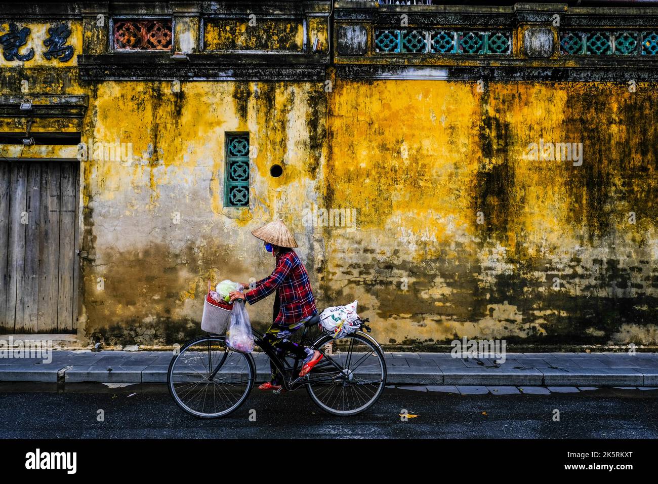 A female cyclist rides a bike along the road in the old town of Hoi An ...