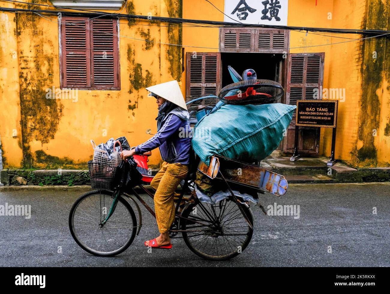 A female cyclist rides a bike along the road in the old town of Hoi An ...