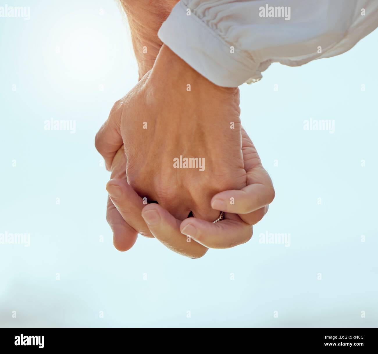 Closeup of a mature couple holding hands and enjoying a romantic stroll together on vacation at the beach. Older couple holding hands outside Stock Photo