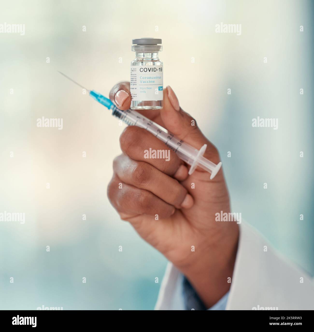 Hand of a doctor holding a bottle of covid vaccine. Medical specialist ready to inject the covid cure. Doctor holding a needle and covid vaccine Stock Photo