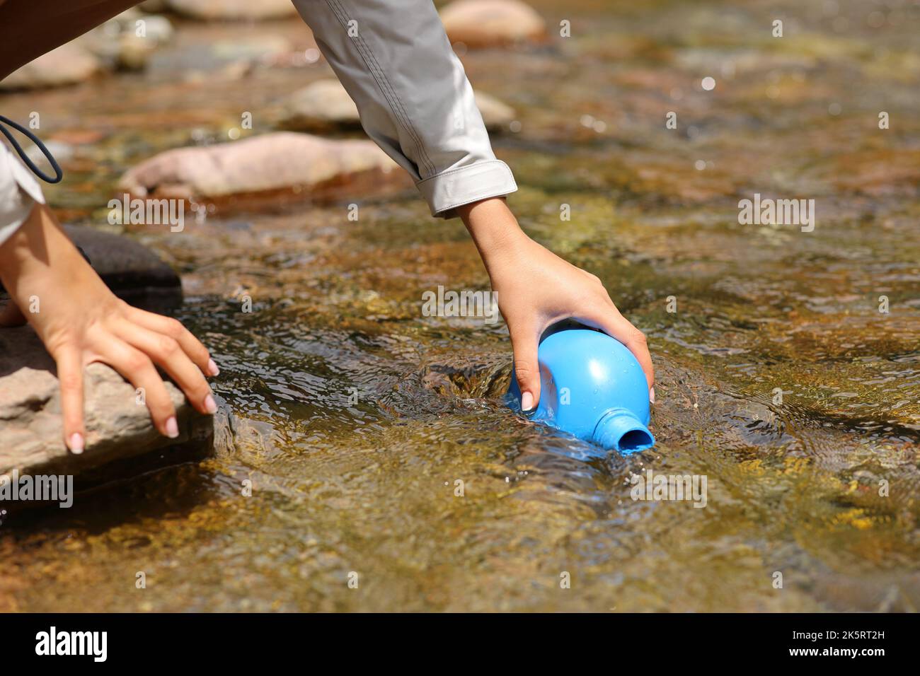 Close up of a hiker hand filling canteen with raw water from river
