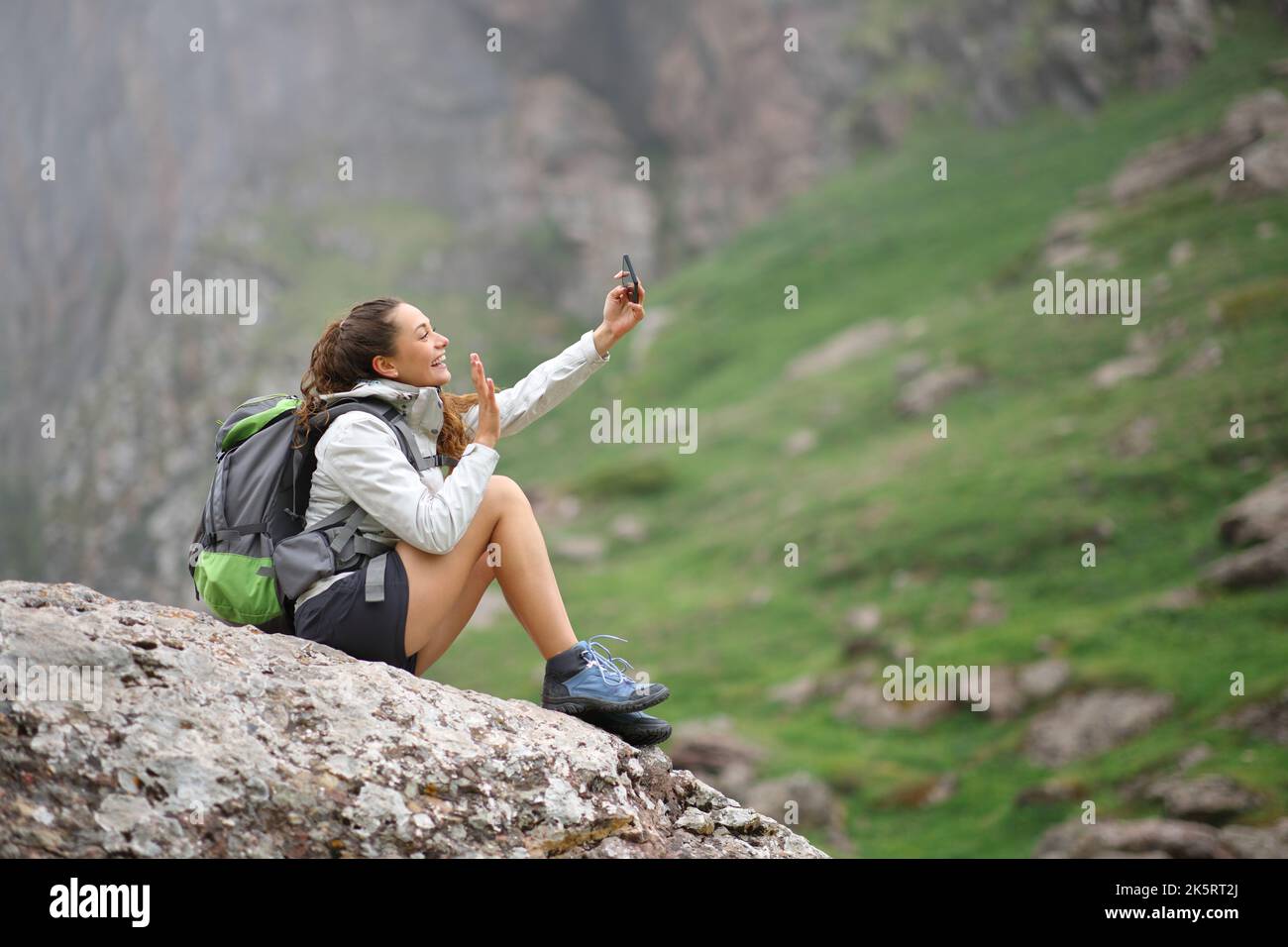 Happy hiker taking selfie with smart phone on a rock in the mountain Stock Photo