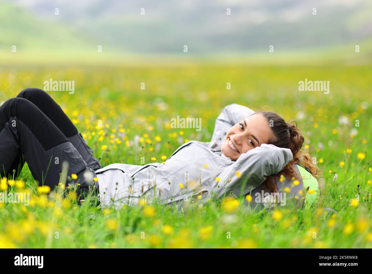 Happy hiker resting lying on the grass looks at you in the mountain Stock Photo