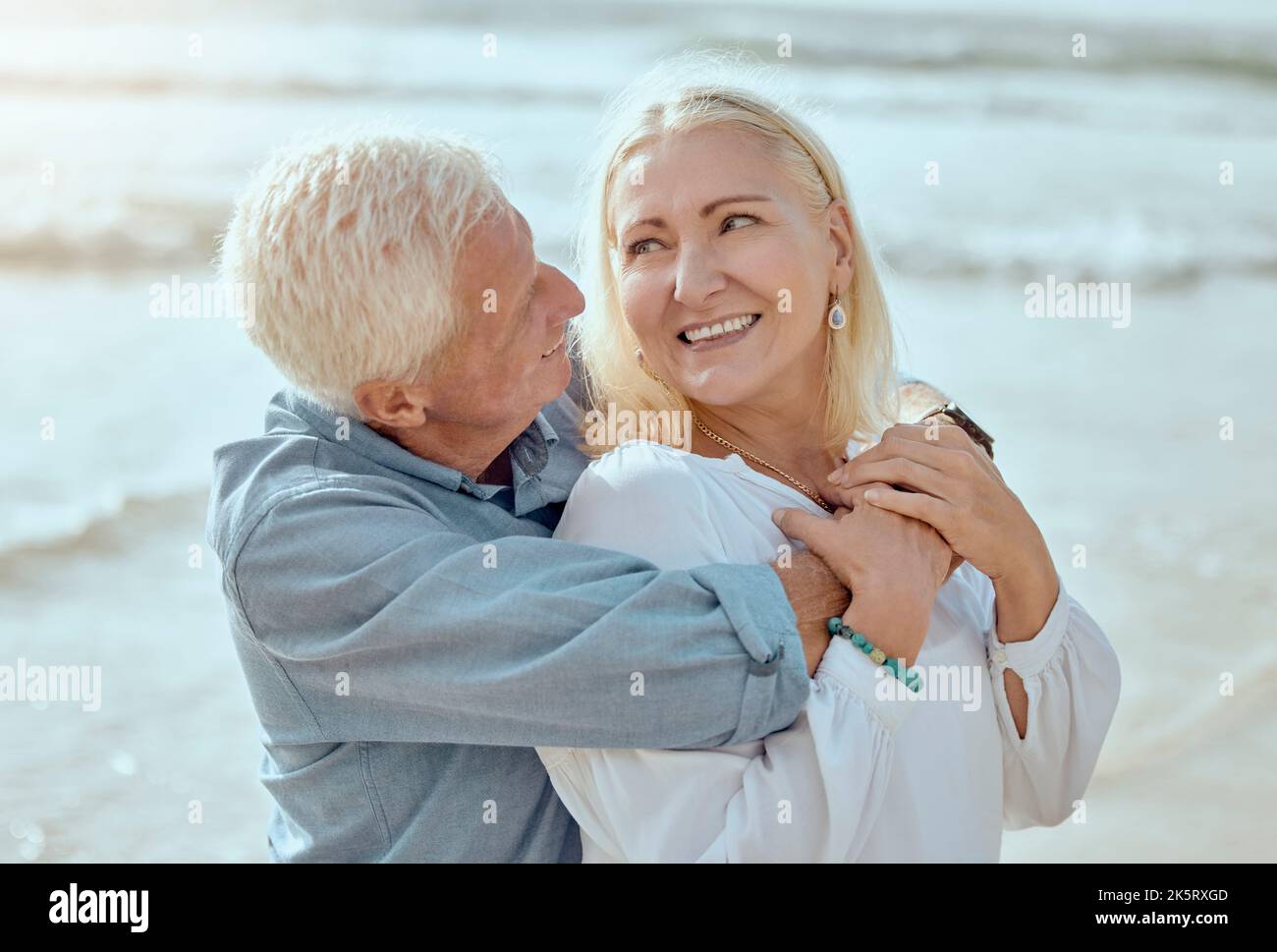 A happy mature caucasian couple enjoying fresh air on vacation at the beach. Smiling retired couple hugging and embracing while bonding outside Stock Photo