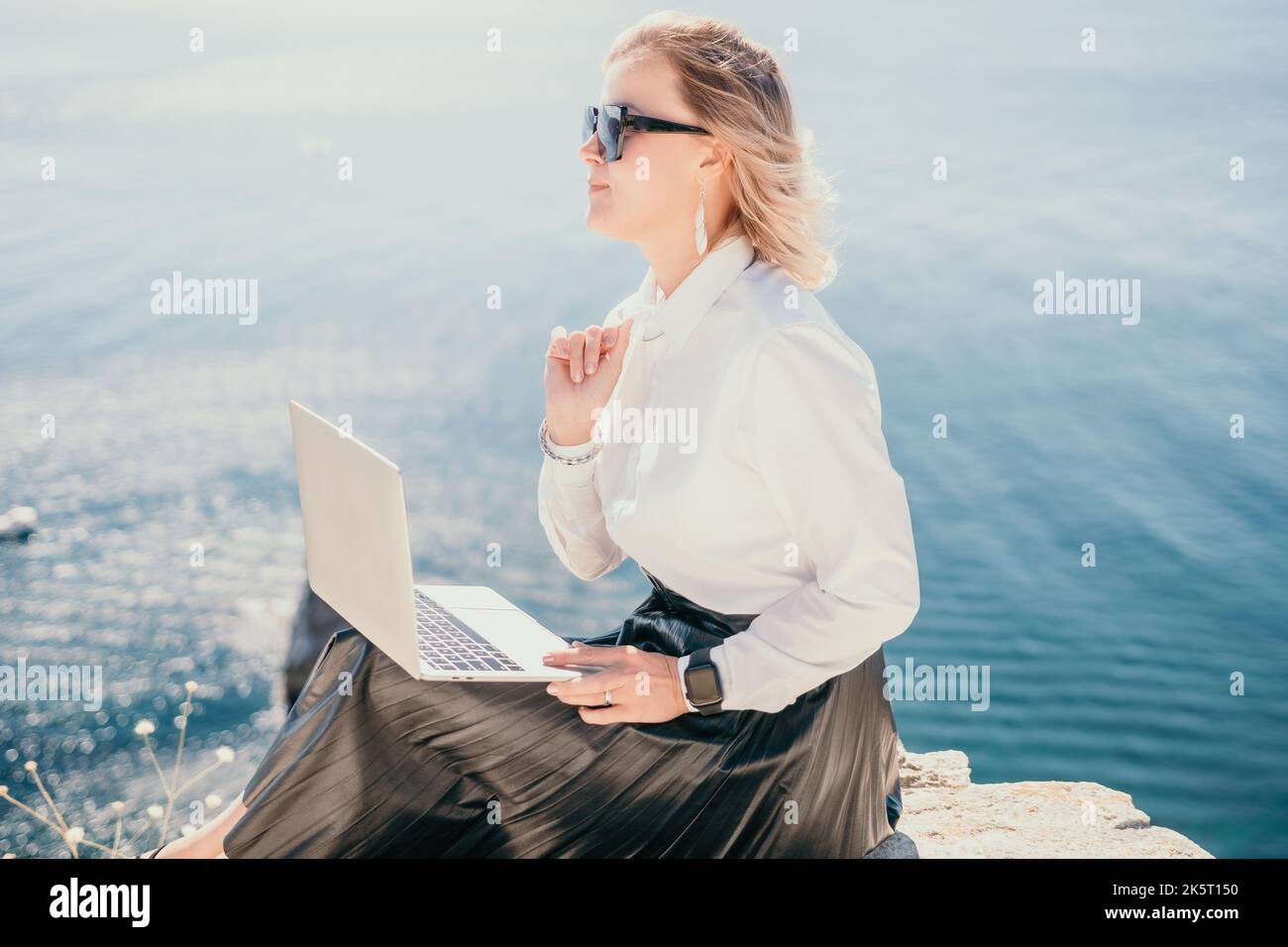 Digital nomad, Business woman working on laptop by the sea. Pretty lady typing on computer by the sea at sunset, makes a business transaction online Stock Photo