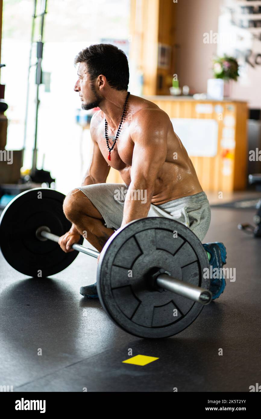 Man resting in a gym while holding a bar with weights Stock Photo