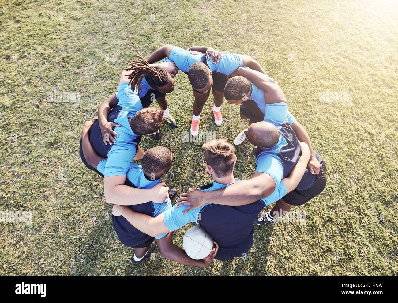 Above diverse group of rugby players standing in a huddle together outside on a field. Young male athletes looking serious and focused while huddled Stock Photo