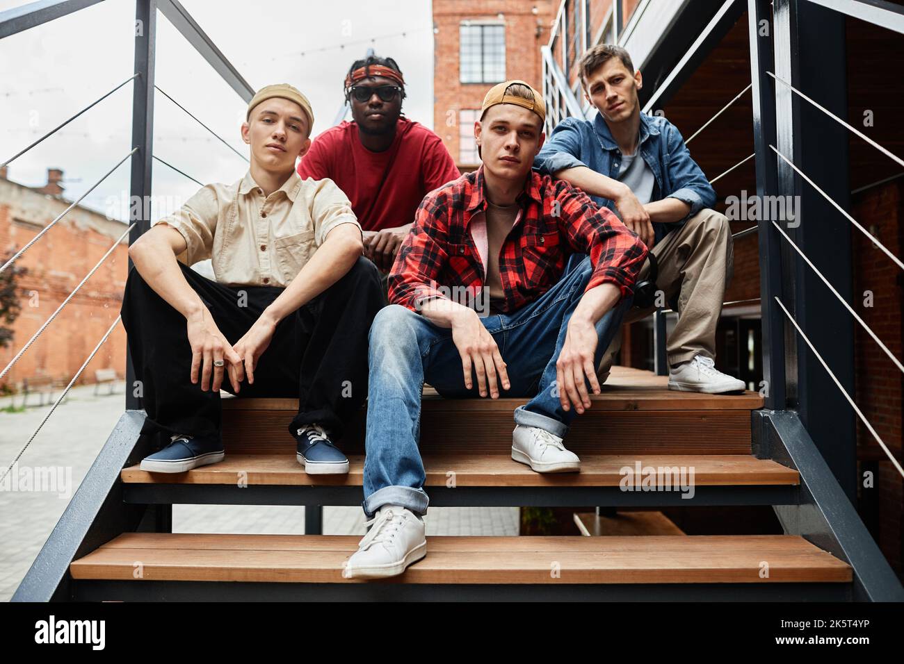 Diverse group of boys wearing street fashion while posing on metal stairs in urban setting Stock Photo