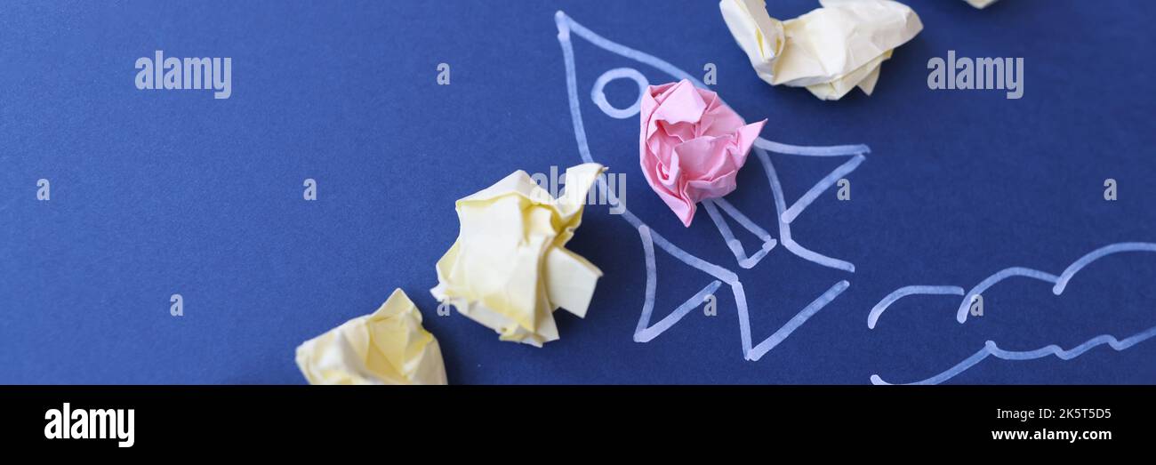 Lot of crumpled papers lying on blue paper with painted rocket Stock Photo