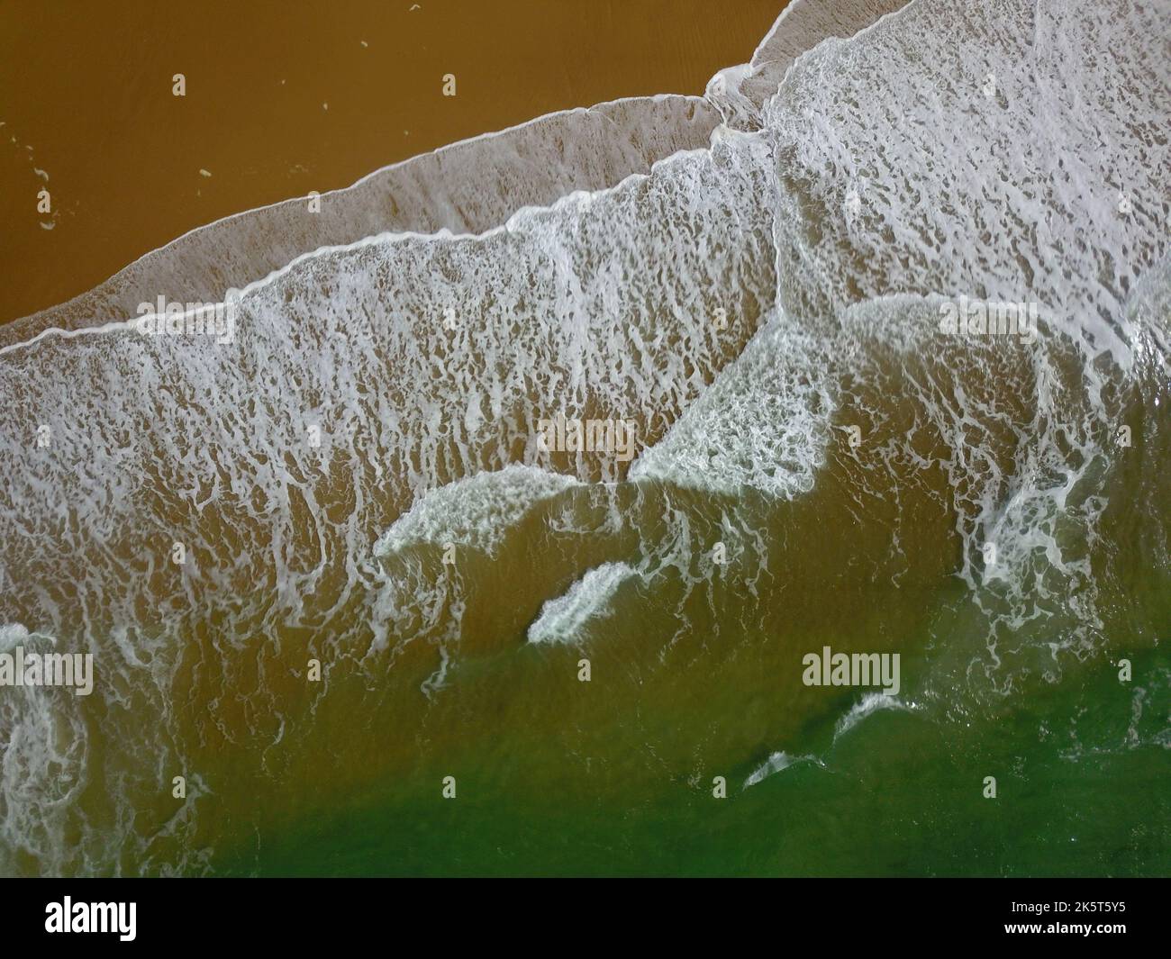 Aerial view of a wide sandy beach with large arriving and breaking