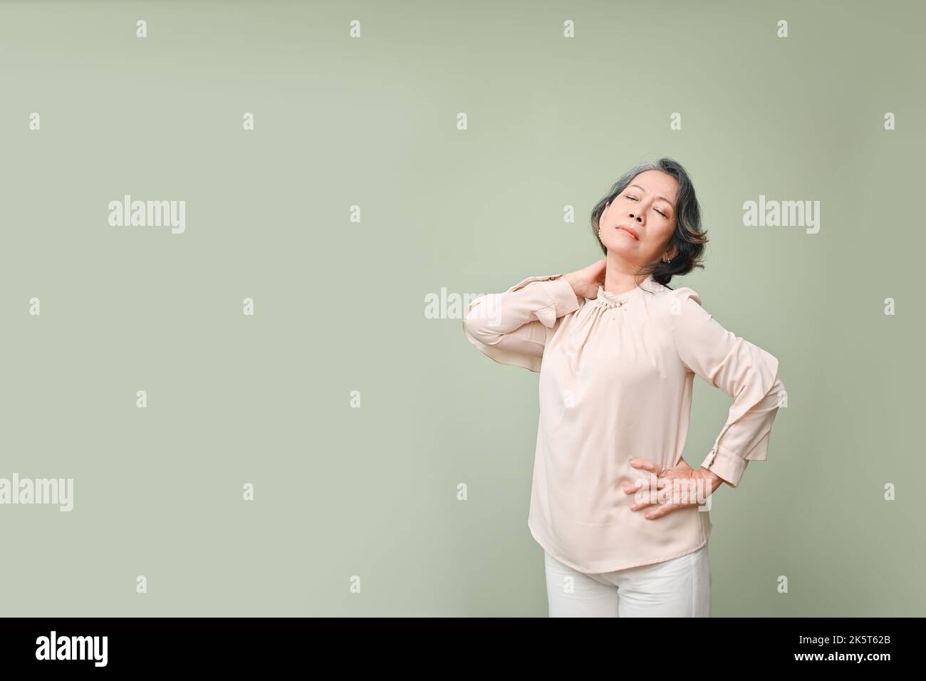 Tired senior Asian woman in casual clothes suffering from her neck pain ...