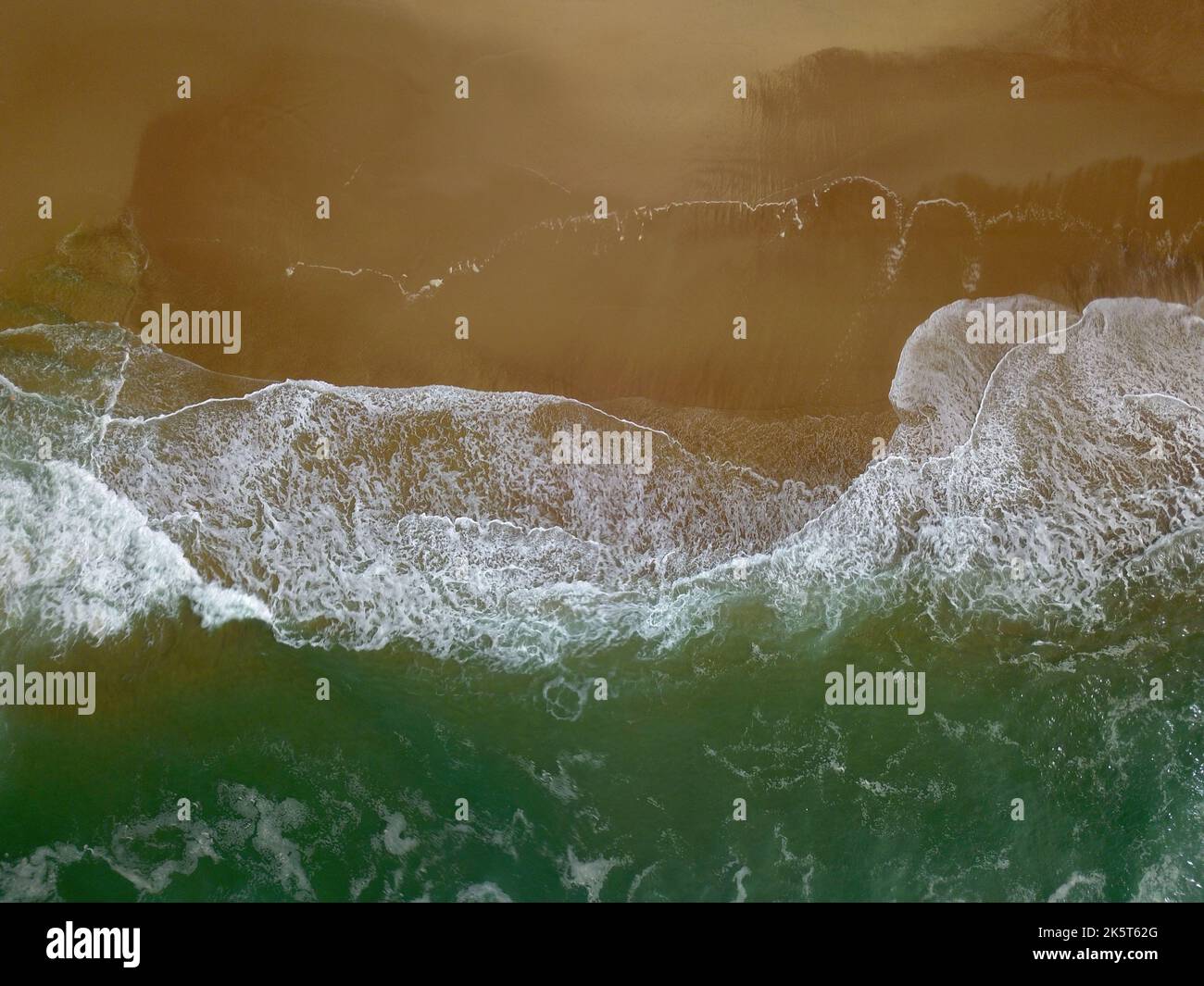 Aerial view of a wide sandy beach with large arriving and breaking