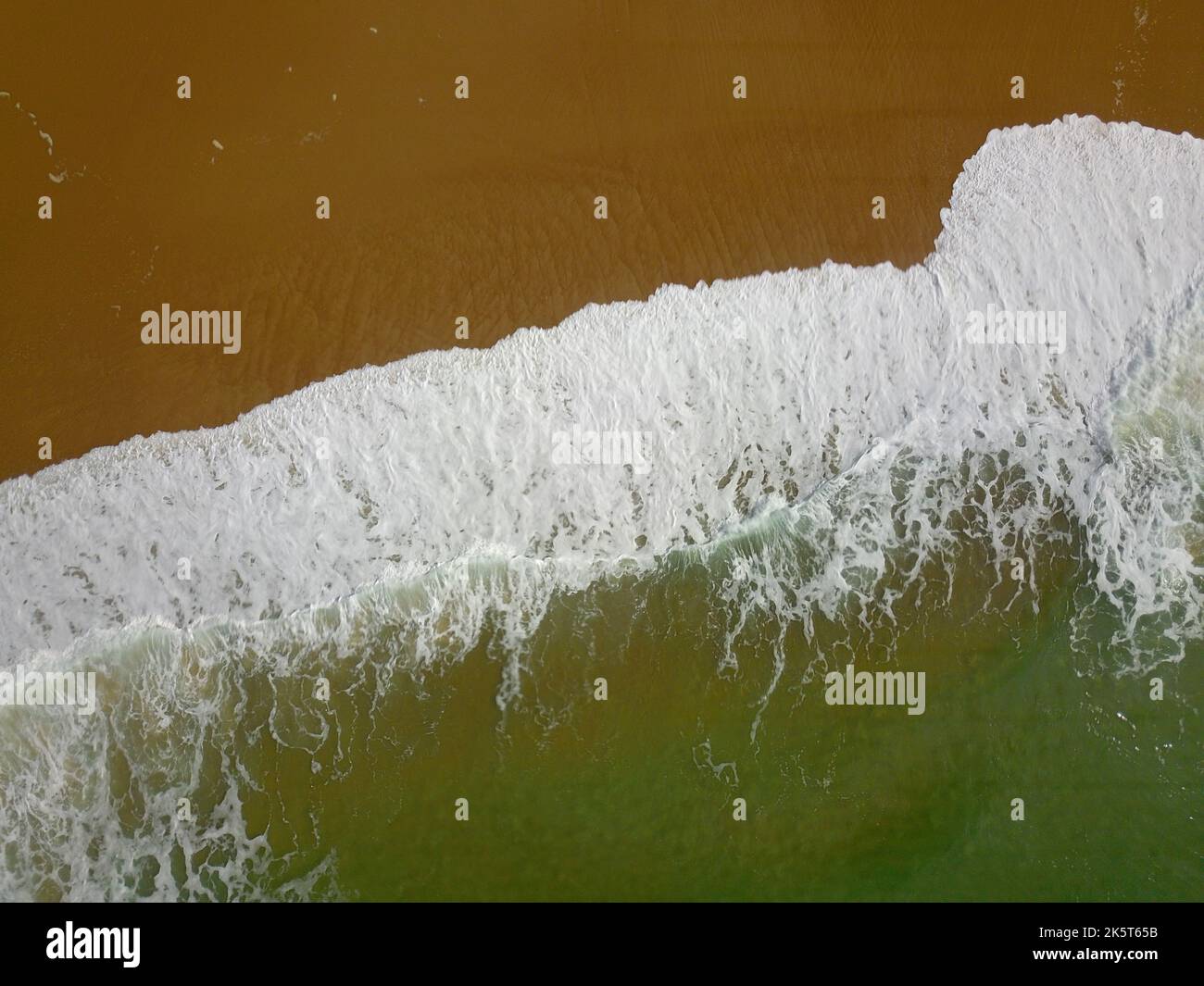 Aerial view of a wide sandy beach with large arriving and breaking