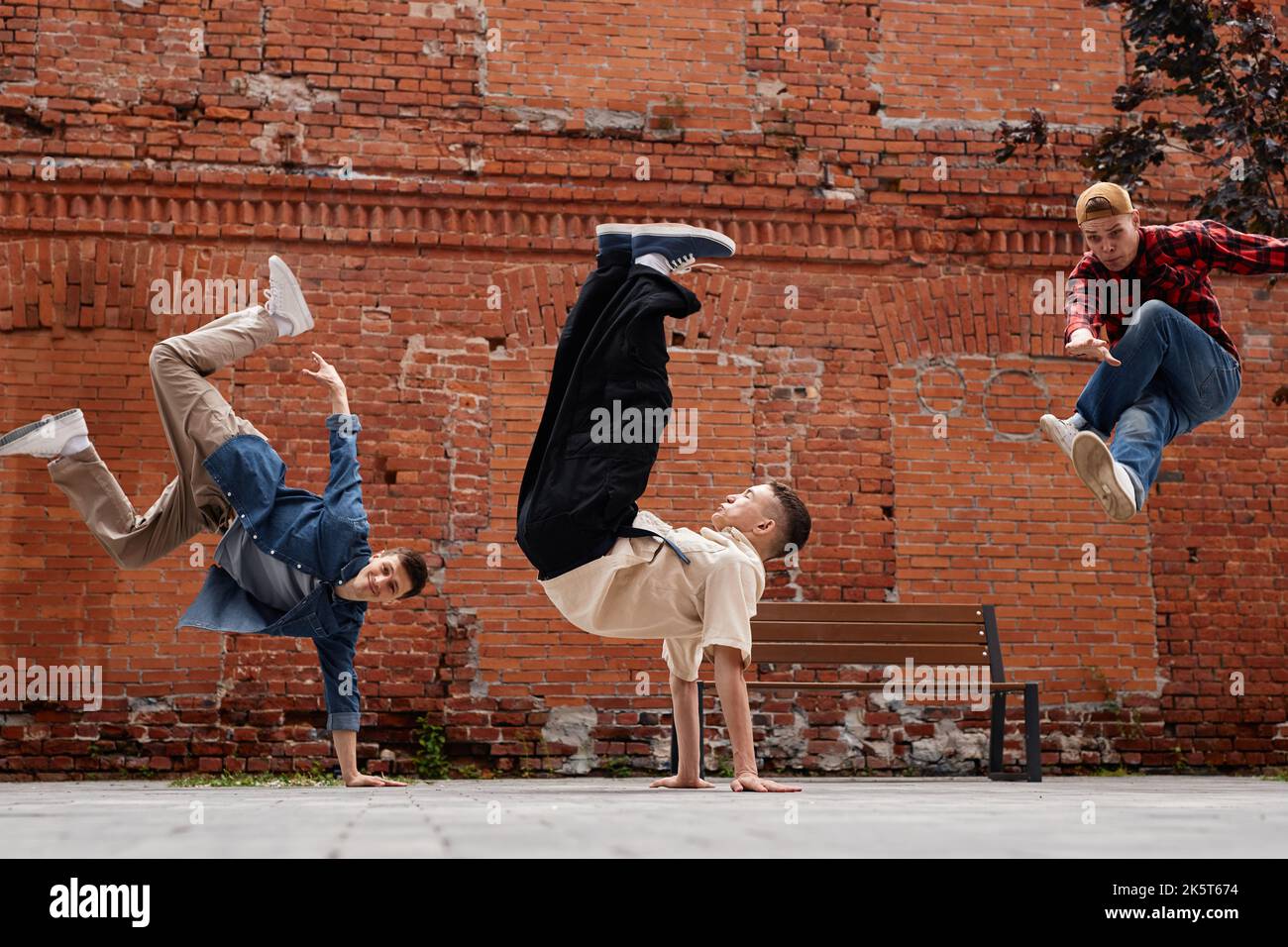 Freeze frame of all male breakdancing team jumping in air against brick wall outdoors Stock Photo