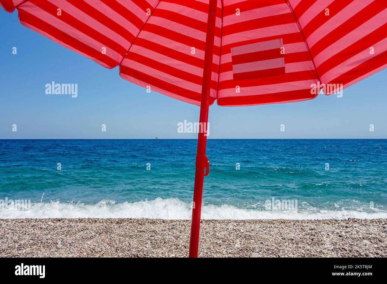 Blue sea, blue sky and a red umbrella - the summertime view from the beach at Fondachello, near Catania, Sicily, Italy Stock Photo
