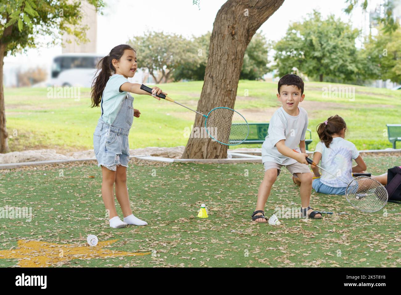 Children playing badminton in park. Young pretty girl and boy playing badminton on summer day. They are about to serve the birdie over the net and so they have a look of concentration on their face. Stock Photo